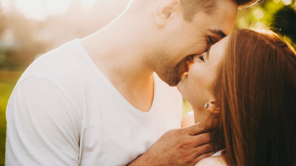 Close up portrait of a modern young couple embracing and kissing while smiling outside against sunset