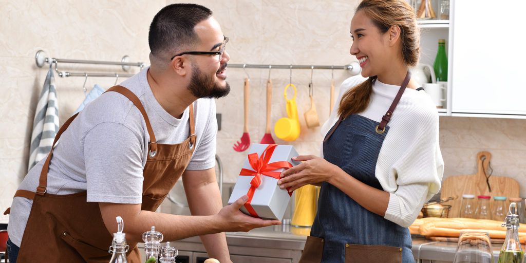 Young asian couple exchanging a gift while cooking in their home kitchen