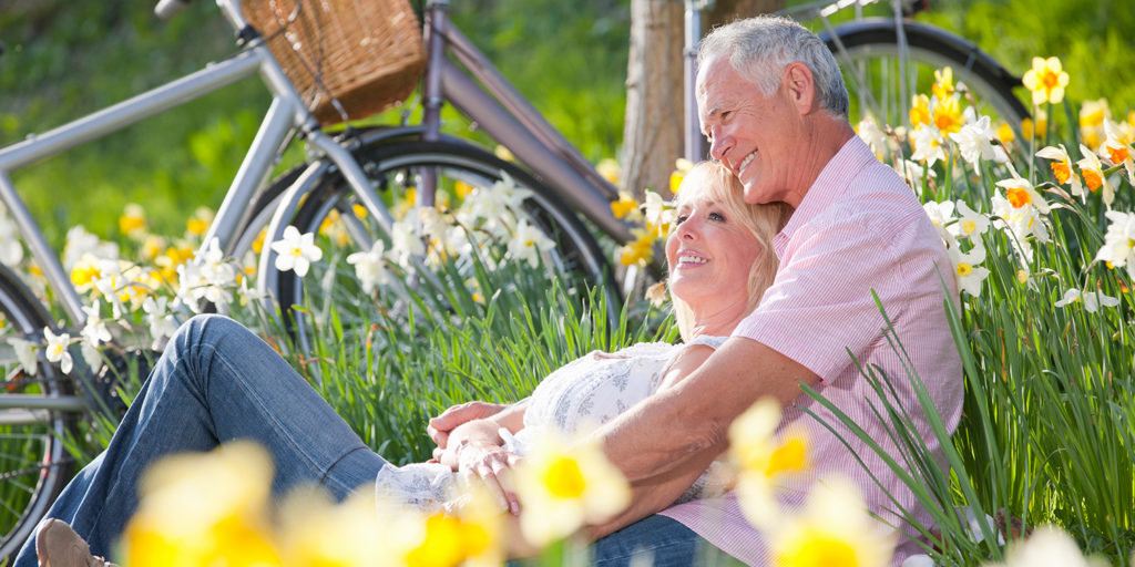 Low angle shot of a seated older white couple cuddling in a daffodil field with their bicycles parked in the background