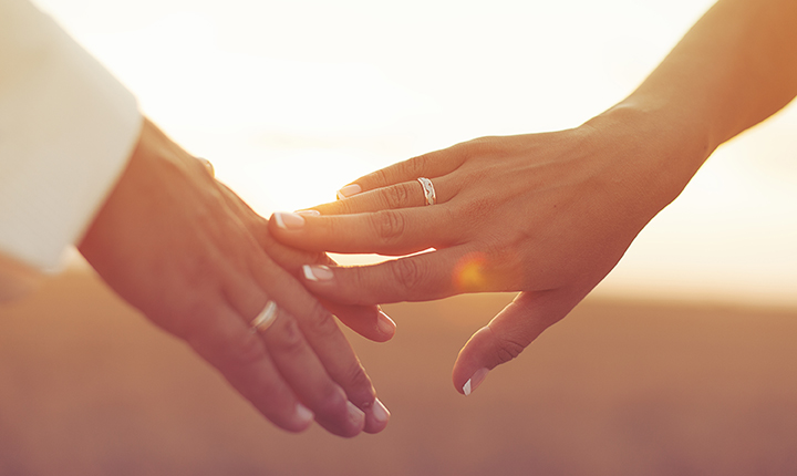 Close up of married couple holding hands with a sunset in the background