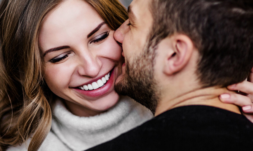 Close up of a man giving his smiling wife a kiss on the cheek