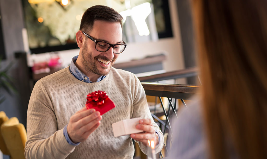 Smiling man opening a gift wrapped box from his wife in a restaurant