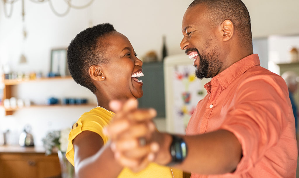 Candid image of a married couple laughing and dancing in their kitchen with adoring expressions