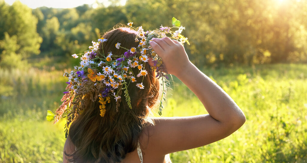 Woman wearing a flower crown in green sunny meadow, rear view, celebrating summer solstice.