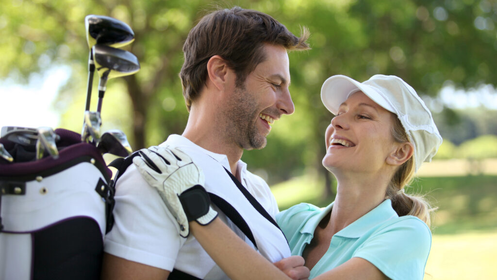 Close up image of a couple embracing on the golf course while smiling at each other.