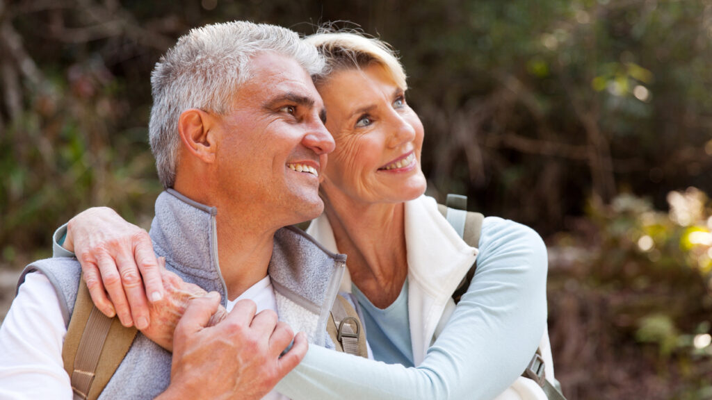 Close up image of an older couple embracing and looking away from the camera while on an outdoor hike 
