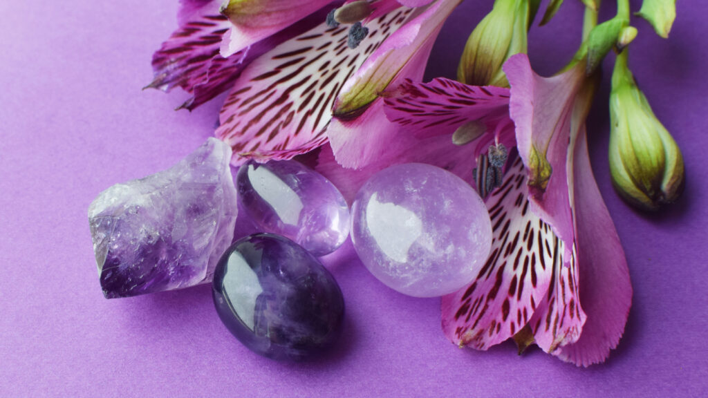 Amethyst crystals, rock crystal, rose quartz and alstroemeria flowers on a purple background.