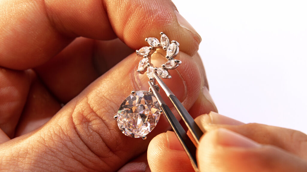 Closeup of a jeweler's hands adjusting a diamond earring with professional tools. 