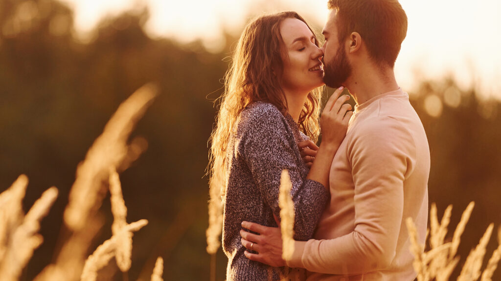 anniversary gifts featured image of a candid caucasian couple in an outdoor field at sunset lovingly embracing and kissing each other.