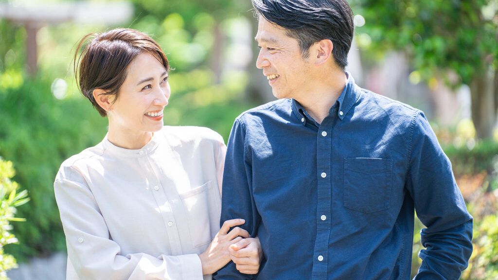 Middle aged asian couple walking arm in arm on an outdoor path while smiling at each other