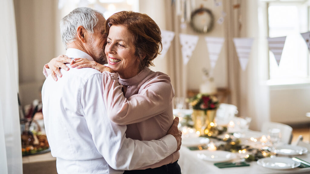 Featured image for 50th wedding anniversary gift ideas - a senior couple standing and embracing in a room set up for their 50th wedding anniversary party.