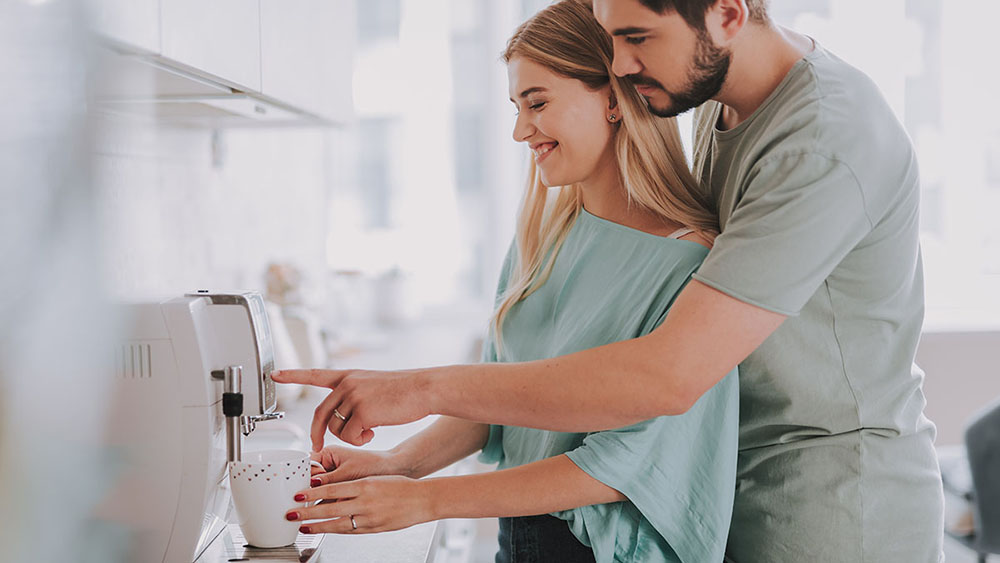 Waist up photo of happy young couple making coffee with machine at home