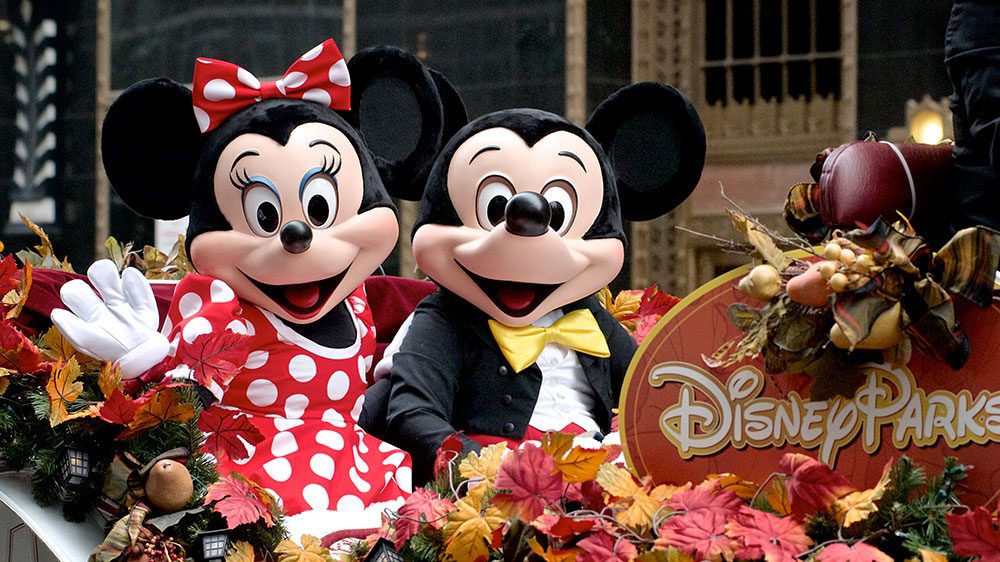 Photo of Mickey and Minnie Mouse characters  waving at the camera seated in a float in a Disney Park parade