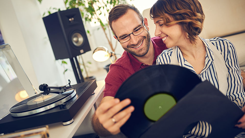 Candid photo of a couple smiling at each other while picking a vinyl record to play in their living room
