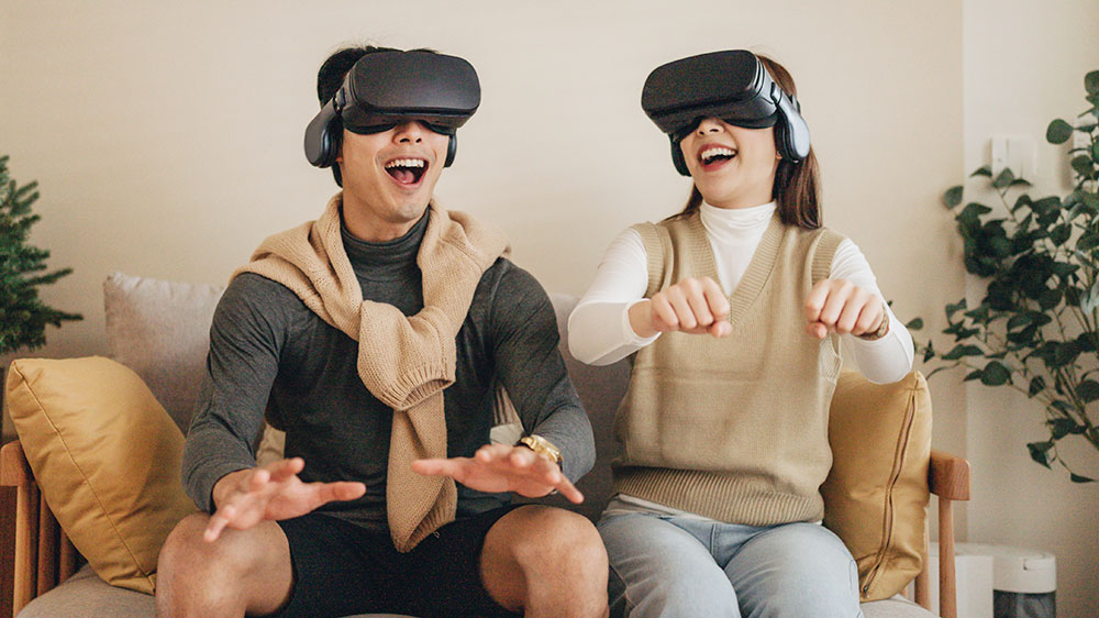 Young smiling couple seated on a couch wearing VR headsets