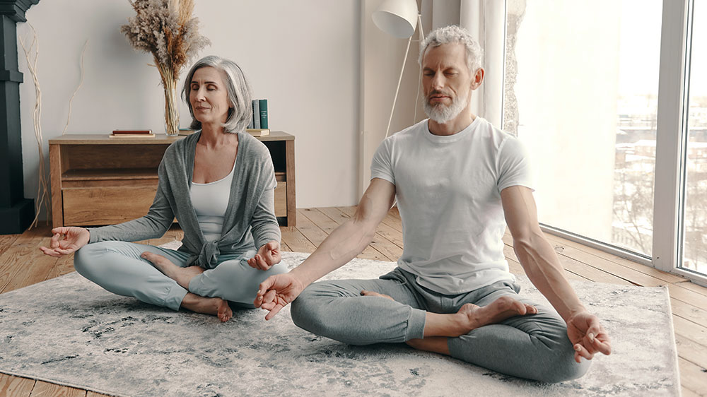 Older couple seated cross-legged meditating in their living room