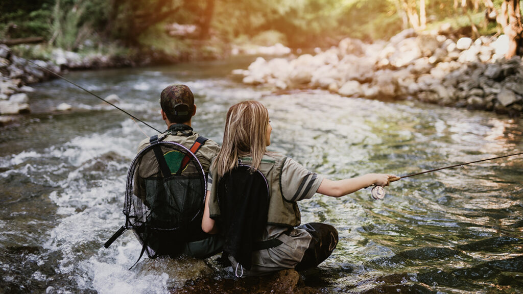 Young adult couple fly fishing together on fast mountain river. 